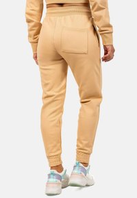 Beige joggingbroek met een relaxed fit, geribbelde tailleband, zijzakken en omgeslagen broekspijpen, gedragen met multikleurige sneakers.