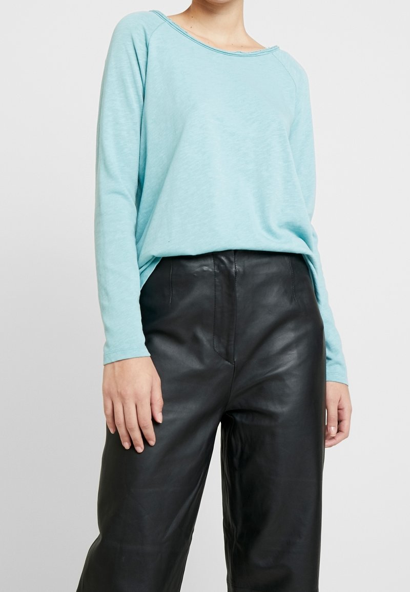 Light blue long-sleeve shirt with a loose fit and wide neckline, paired with high-waisted black leather pants, structured yet soft texture.