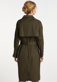 Płaszcz trencz w oliwkowej zieleni z paskiem, długimi rękawami, bocznymi kieszeniami i warstwowym tyłem. Gładka tkanina o lekkim połysku.