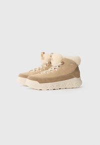 Botas de tobillo de ante beige con un lujoso cuello de forro de lana crema, cuentan con ojales de metal, cordones planos y una suela de goma blanca texturizada.