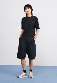 Black athletic short-sleeve top with gray stitching, paired with loose-fitting black shorts, and metallic sneakers. Smooth texture.