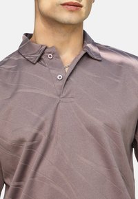 Koszulka polo z krótkimi rękawami w kolorze mauve z teksturowanym wzorem fali, z dwoma guzikami na plisce oraz luźnym kołnierzykiem.