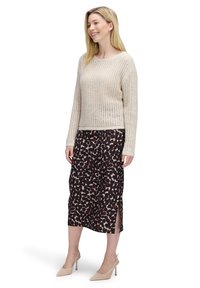 Hellbeige gestrickter Pullover mit lockerer Passform. Dunkel gemusterter Midirock mit Schlitzen. Beigefarbene Absatzschuhe runden das Outfit ab.