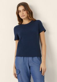 Tricou bleumarin cu mânecă scurtă, fabricat dintr-un material neted, având un guler rotund și o croială lejeră, asortat cu pantaloni cargo din denim.