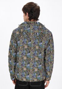 Giacca a cappuccio colorata con sfondo nero e un motivo dettagliato di simboli di gioco in giallo, blu e rosa. Il materiale sembra leggero.