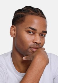 Headshot of a person with braided hair, smooth skin, a subtle earring, and a thoughtful expression, wearing a plain white T-shirt.