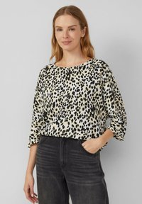 Leopardenmuster-Bluse in Beige und Schwarz, mit rundem Ausschnitt und Dreiviertelärmeln, kombiniert mit dunkelblauen Jeans.
