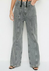 Jeans de tiro alto y pierna ancha en denim gris claro. Presenta líneas verticales cosidas y un cierre con cordón. Incluye bolsillos laterales.