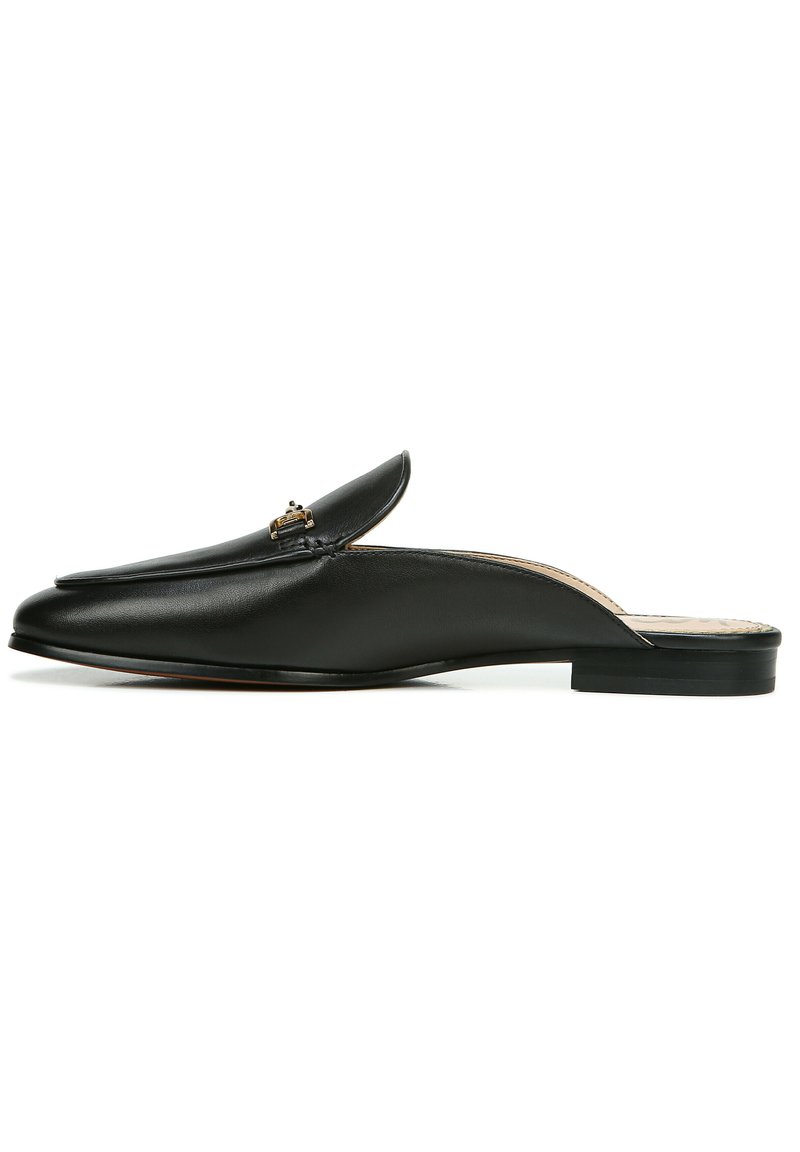 Chaussure slip-on en cuir noir avec un pied pointu, un petit talon et un accent doré décoratif sur le dessus. Texture lisse et design minimal.