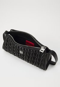 Sac noir en cuir tressé avec fermeture éclair, dotée d'une étiquette de logo rouge à l'intérieur et d'un accent en métal argenté. Design compact et structuré.