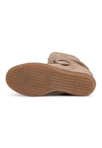 Bottes en daim beige présentées semelle vers le haut, avec une semelle en caoutchouc texturée arborant un motif géométrique d'étoiles et deux bandes horizontales antidérapantes.