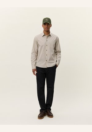 Beige kariertes Hemd mit Knopfleiste, kombiniert mit einer dunklen Hose und braunen Schuhen. Grüner Hut mit Logodetail. Schlichtes, sauberes Design.