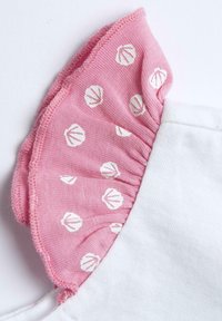 Indumento bianco con un colletto arricciato rosa che presenta motivi a conchiglia bianchi, mettendo in risalto i colori contrastanti e il tessuto testurizzato.