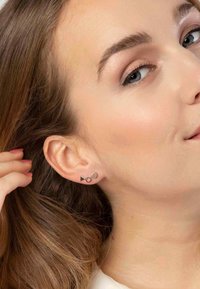 Zilveren studs met driehoekige, ronde en ovale vormen, gedragen in het oor van een model met lichtbruin haar dat gedeeltelijk bedekt is.