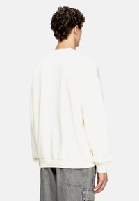 Sudadera oversized de color crema claro con cuello redondo y hombros caídos. Tejido suave y puños acanalados, combinada con pantalones cargo grises.