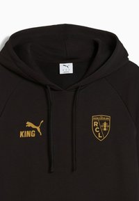 Felpa nera con cappuccio realizzata in tessuto morbido, con loghi dorati: Puma sul lato sinistro del petto e "KING" sotto, più l'emblema del Racing Club de Lens sulla destra.