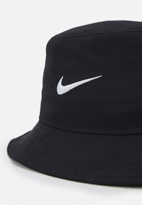 Černý klobouk s širokým krempou, vyrobený z textilu, na přední straně s bílým vyšívaným logem Nike. Krempa má široký a strukturovaný povrch.