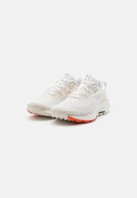 White athletic shoes with mesh upper, textured detailing, and orange rubber outsole. Features traditional lacing and brand logo on tongue.