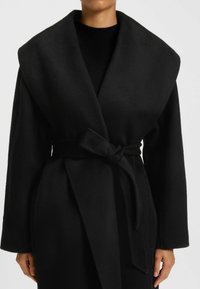Black wrap coat made of soft fabric, featuring a wide collar, long sleeves, and a tie belt detail for closure. Smooth texture.