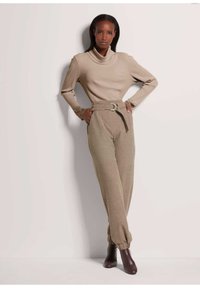 Beige geribbelde coltrui met kanten accenten op de mouwen, gecombineerd met hoge beige broek en bordeauxrode enkellaarsjes.