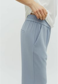 Light blue casual pants with an elastic waistband, side pockets, and a smooth texture, shown from the side with a white top partially visible.