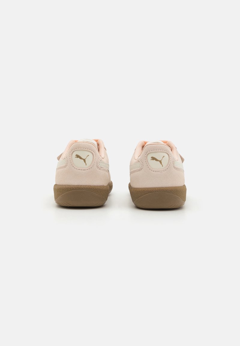 Baskets en daim rose clair avec une semelle en caoutchouc marron, présentant un logo en or au niveau du talon et des accents roses autour du col.
