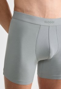 Sloggi boxerky v světle šedé barvě, vyrobené z hladkého materiálu, s minimalistickým designem, elastickým pasem a jemnými detaily šití.