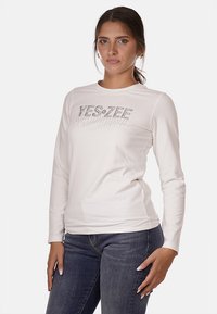 T-shirt bianco a maniche lunghe con una grafica "YES-ZEE" in strass argentati sul petto. Realizzato in un morbido tessuto misto cotone.