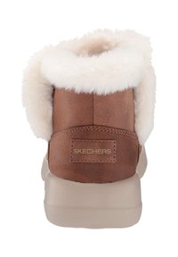 Brown suede ankle boots with a white fur-lined collar, featuring a beige rubber sole and embossed "SKECHERS" logo on the back.