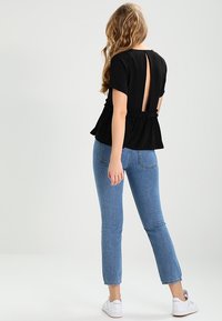 Top peplum negro con un corte en forma de ojal en la espalda, con dobladillo fruncido; combinado con jeans rectos de color azul claro y zapatillas blancas.