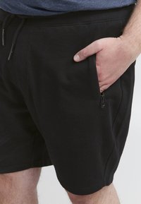Shorts de sport noirs en mélange de coton, dotés d'une poche latérale zippée et d'une taille élastique avec cordon de serrage.