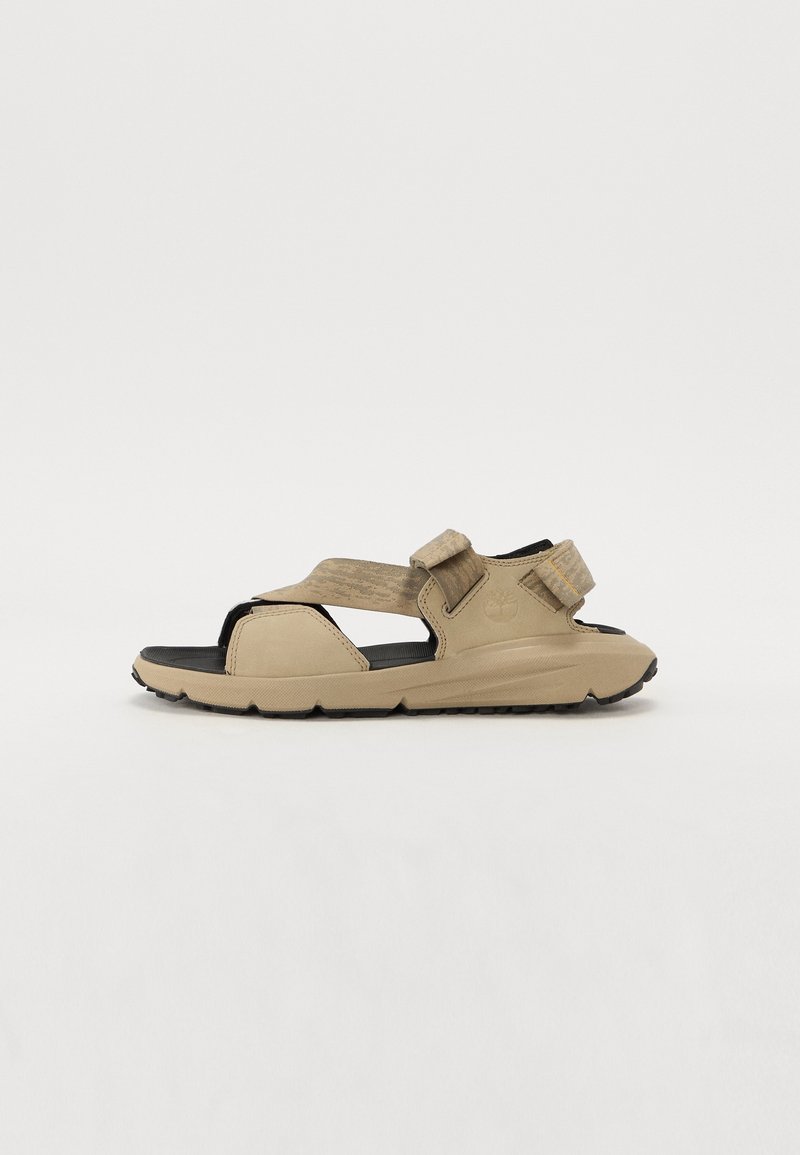 Sandale beige à bout ouvert avec deux brides réglables, semelle noire rembourrée et semelle extérieure robuste, vue de côté sur fond blanc.