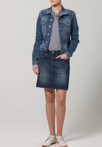 Jeansjacka med knappstängning och två framfickor, kombinerad med en randig skjorta och en mörk jeanskjol. Bärs med vita snörskor.