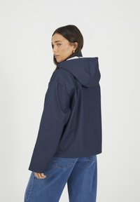 Granatowa wodoodporna kurtka z kapturem, charakteryzująca się luźnym krojem, gładką teksturą i kontrastowym podszewką. Widoczne szwy i detale rękawów.