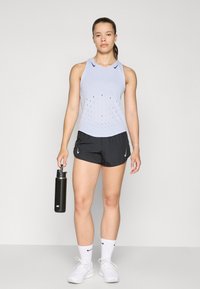 Lyseblå atletisk tanktop med perforeret design, parret med sorte shorts. Iført hvide sneakers og holder en sort vandflaske.