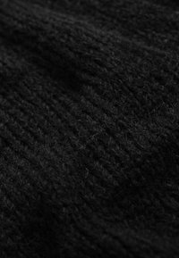 Czarna dziana tkanina o miękkiej, puszystej fakturze. Wzór wyróżnia się pionowymi prążkami, tworząc wrażenie warstwowości.