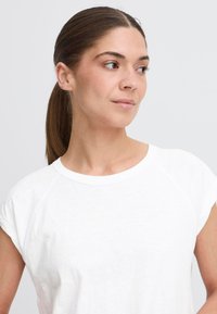 Vit bomulls-t-shirt med korta raglanärmar, rund halsringning och en slät textur. Enkelt design, fokuserad på komfort och mångsidighet.