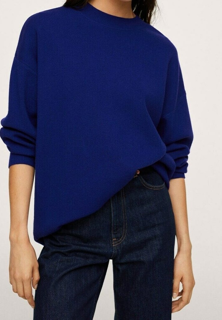 Personne portant un pull ample bleu foncé avec les manches remontées, associé à un jean taille haute bleu foncé sur un fond uni.