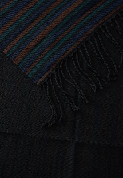 Écharpe tissée rayée aux couleurs noir, marron, vert et bleu, avec des bords à franges torsadées sur un fond de tissu noir uni.