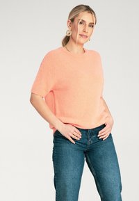 Krótki, puszysty różowy sweter z okrągłym dekoltem, połączony z niebieskimi dżinsami o wysokim stanie. Miękka tekstura i luźny krój.