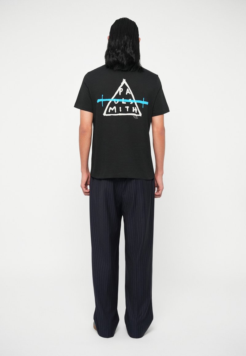 Juodas medvilninis marškinėlis su baltu ir mėlynu trikampio grafiku nugarinėje pusėje, derinamas su tamsiai mėlynomis juostuotomis kelnėmis. Vaizdas iš nugaros.