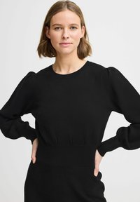 Svart puffärmad tröja med rund nacke och ribbad midja. Tyget ser mjukt ut med en slät textur och minimalistisk design.