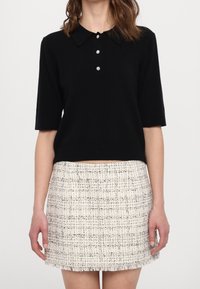 Polo negro de manga corta con botonadura de tres botones y cuello, combinado con una minifalda de tweed crema con borde de flecos.