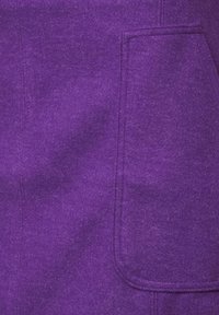 Violetti huopakangas, jossa on ylhäältä ommeltu tasku ja pehmeä tekstuuri. Muotoilu on yksinkertainen, siisteillä linjoilla ja tasaisella värillä.