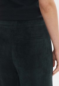 Dark green corduroy pants with a textured surface, featuring a back pocket and a smooth, elastic waistband.
