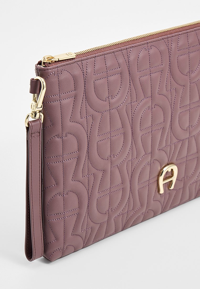Fioletowa torebka typu clutch z pikowanej skóry, z złotymi akcentami, z wyraźnym logo i zapięciem na zamek, zaprojektowana w gładkiej teksturze.