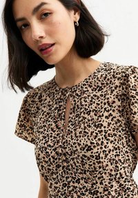 Blusa in stampa leopardata beige e marrone con maniche corte, dettaglio del collo a chiave e leggera arricciatura in vita. Texture liscia.