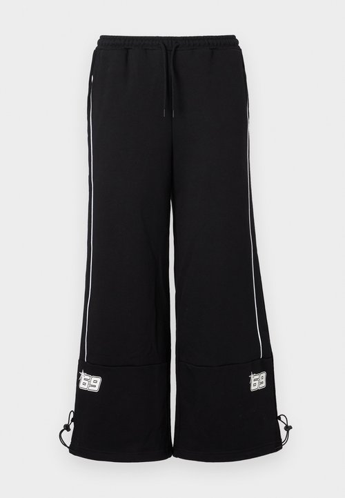 Zwarte wijde joggingsbroek van zacht materiaal, met witte zijstrepen en een logo-label aan de onderzijde, voorzien van verstelbare koordjes bij de manchetten.