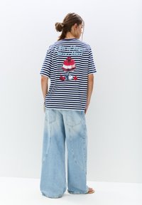 Stribet navy og hvid t-shirt med et stort, farverigt dessertmotiv på ryggen. Kombineret med løse, lyseblå denim jeans.