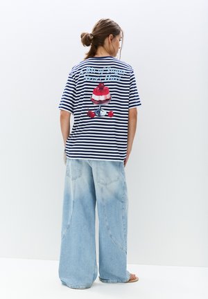Gestreiftes T-Shirt in Marineblau und Weiß mit einer großen, bunten Dessertgrafik auf der Rückseite. Dazu lockere, hellblaue Jeans aus Denim.